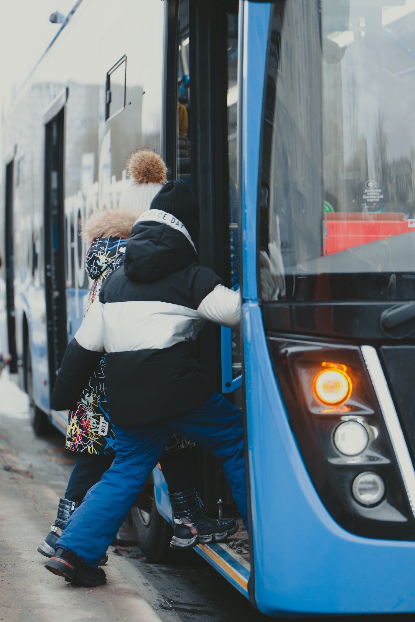 the-girls-enter-the-doors-of-a-blue-bus-that-has-arrived-at-the-bus-stop-.jpg